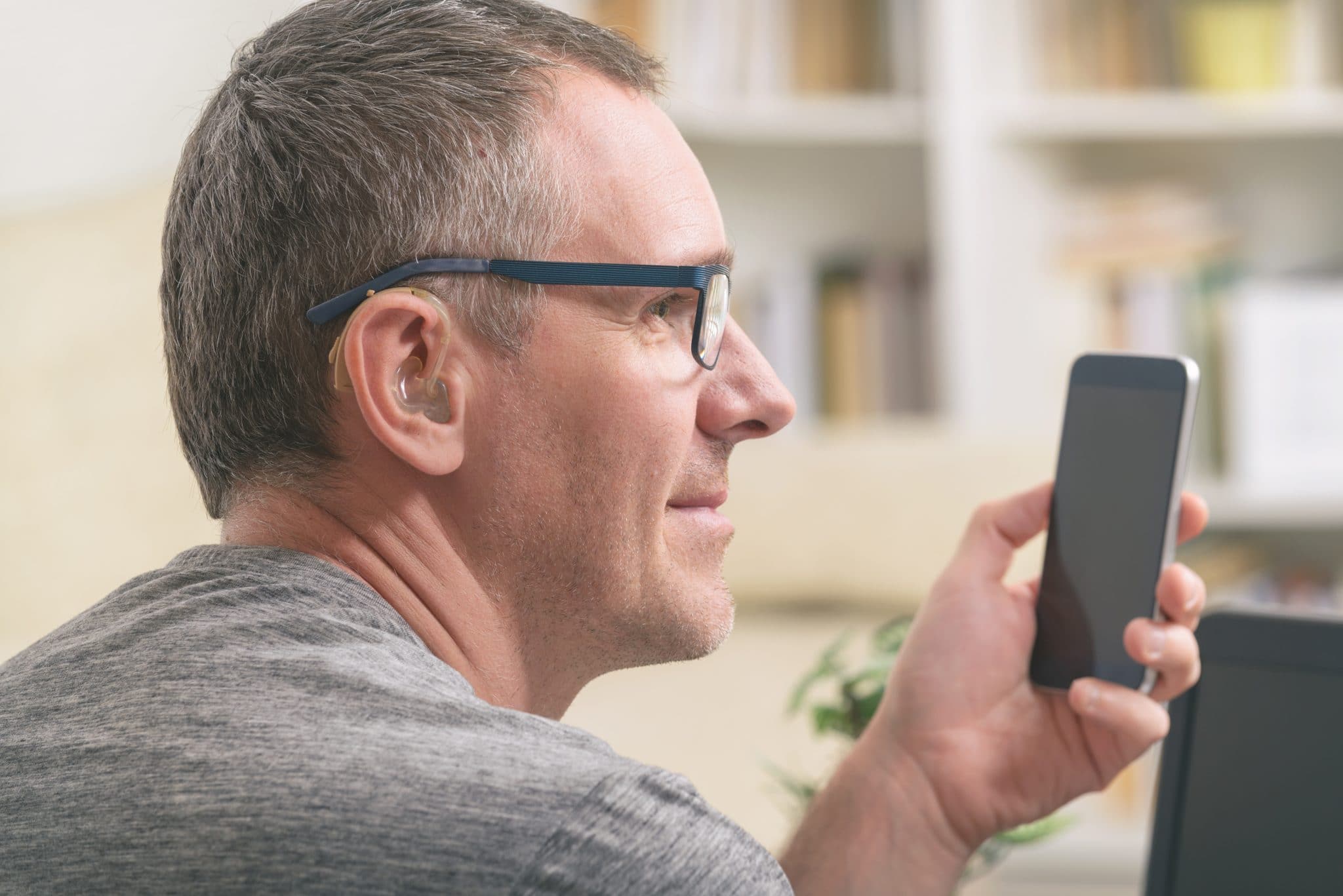 Man with hearing aid looks at phone.