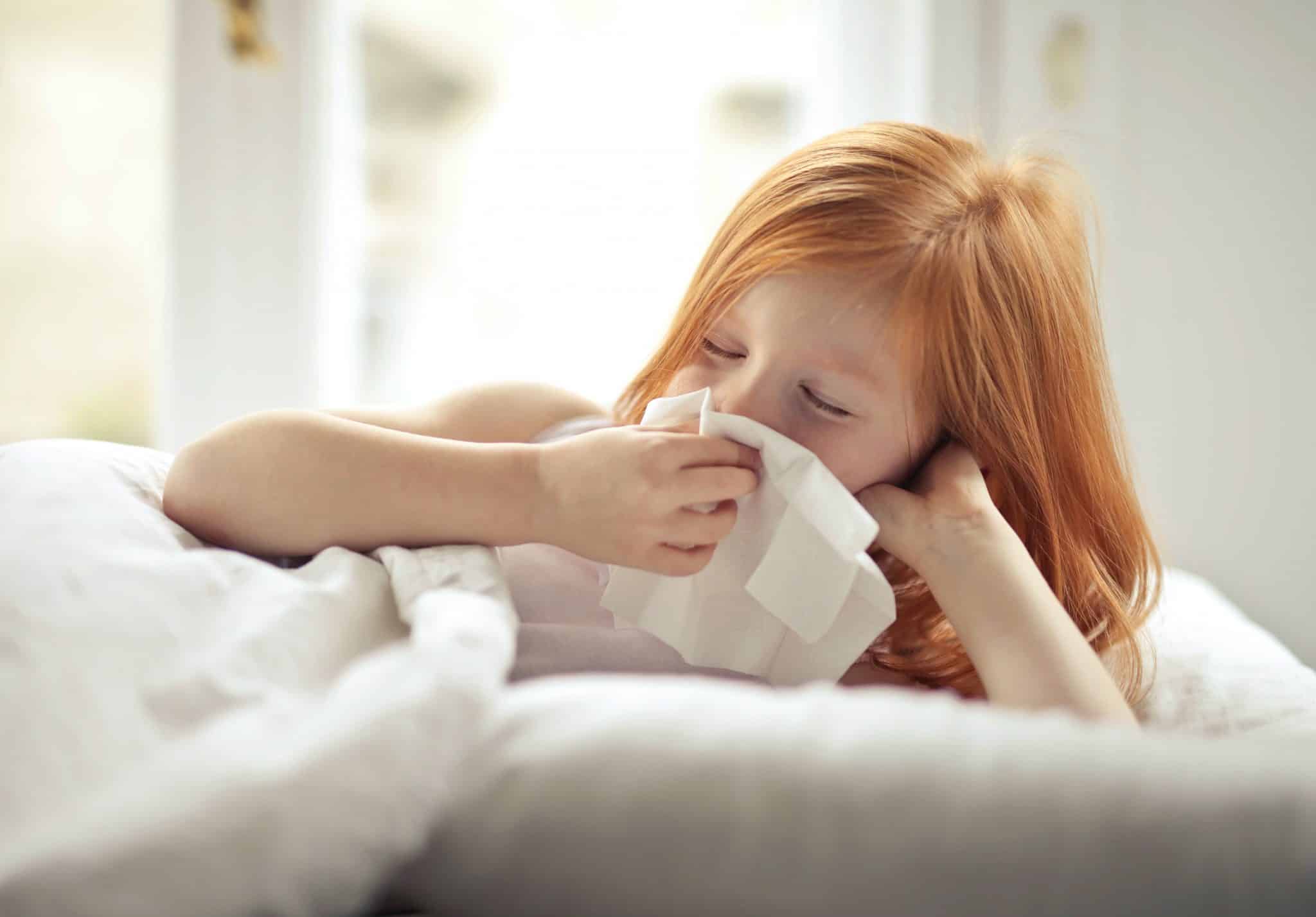 Little girl blowing her nose while in bed.