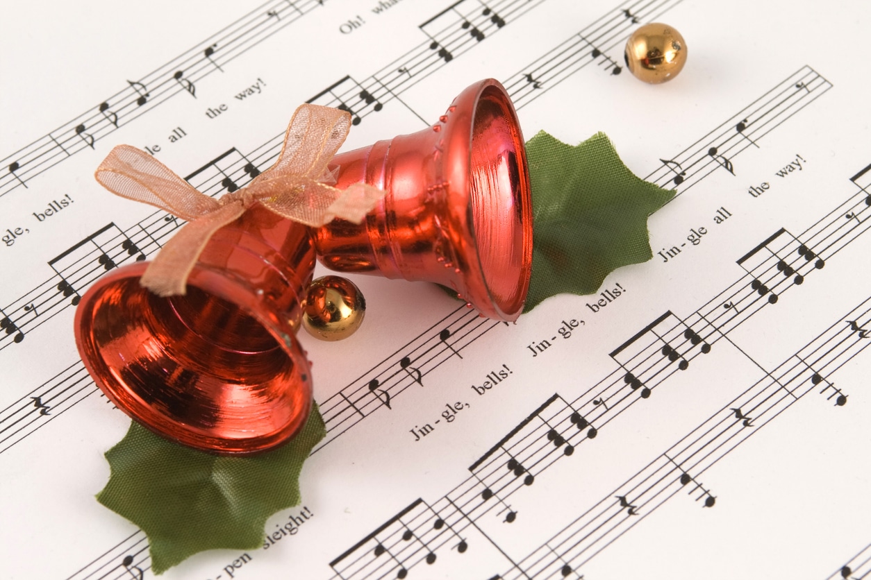 Close up of red holiday bells on top of the sheet music for "Jingle Bells"